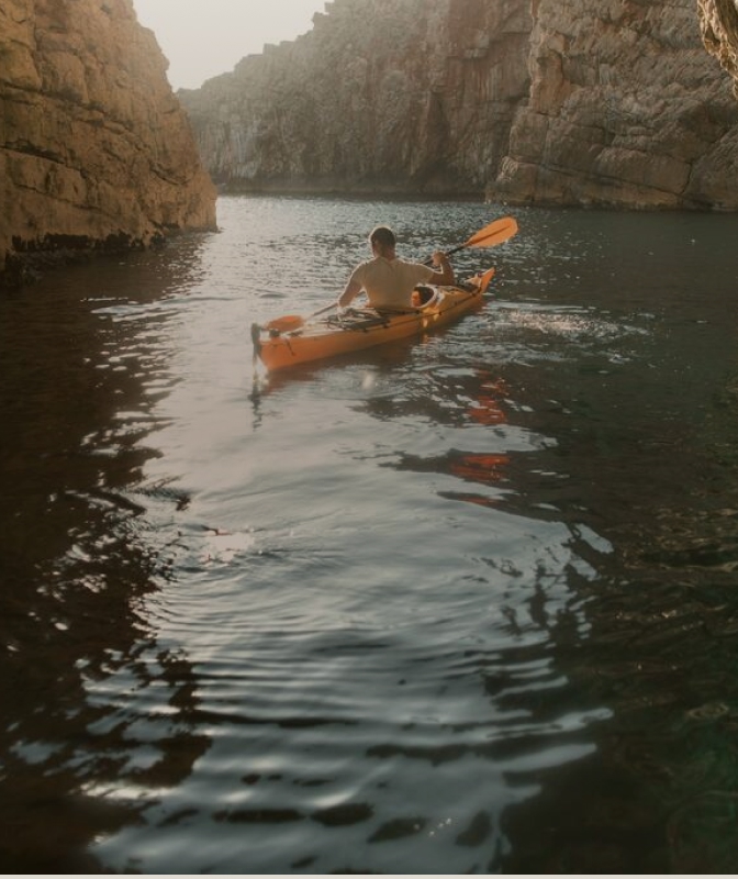 Person paddling a kayak through a narrow canyon surrounded by steep rock walls and calm water